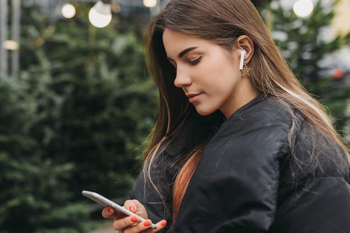 Pretty girl wear black, using phone with head phones, outdoor. Copy space