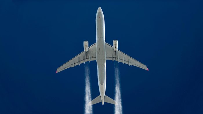 underside of a plane flying. blue sky background. vapor trails.