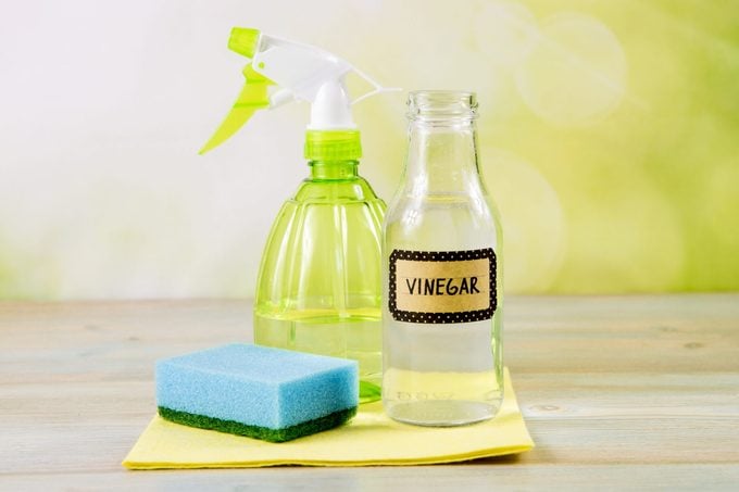 Chemical free home cleaner products concept. Using natural destilled white vinegar in spray bottle to remove stains. Tools on wooden table, green bokeh background, copy space.