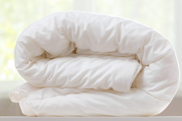 A folded white duvet lies on a table on a blurred background.
