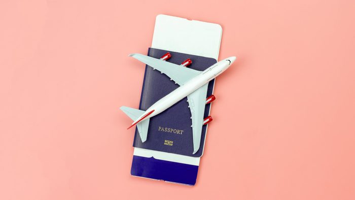 model airplane on a passport with tickets inside. peach background.