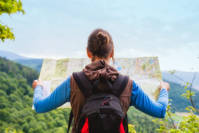 Woman traveler with backpack checks map to find directions in wilderness area, real explorer. Travel Concept