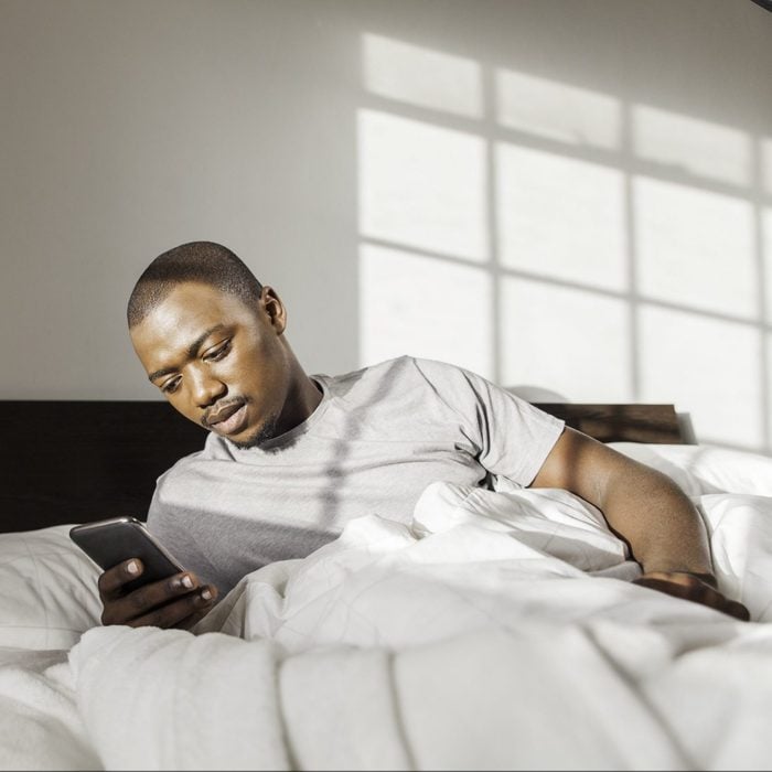 Businessman Waking Up In Bed Texting On His Phone In The Morning.