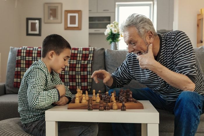Happy little kid playing chess with senior man at home. Family relationship with grandfather and grandson. Grandpa and male grandchild playing board game in the living room