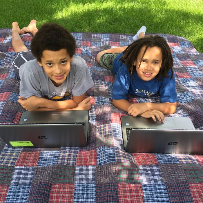homeschooling. laptops on a picnic blanket outside.