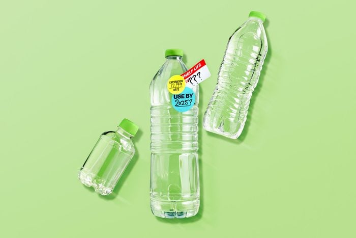 three various plastic water bottles on green background. center bottle has expiration stickers on it