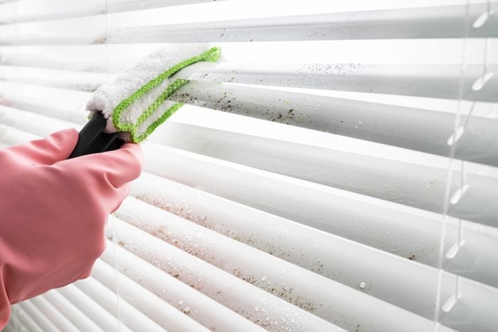 Hands in pink gloves Cleaning dirty blinds with a duster
