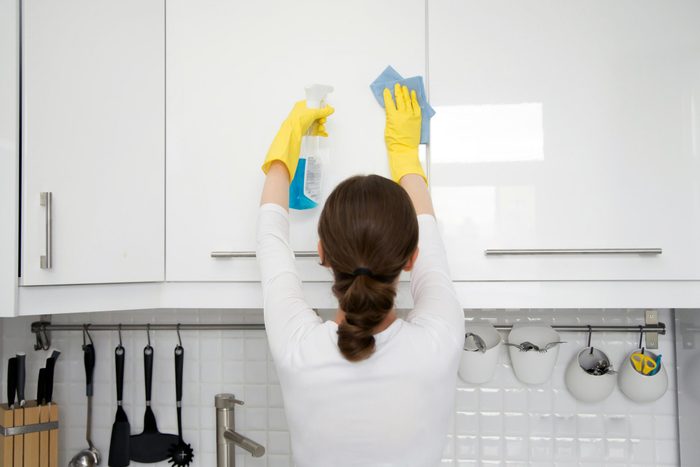 Girl with brown hair cleaning kitchen cupboard doors for spring cleaning