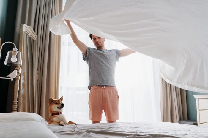 Man making the bed with his dog