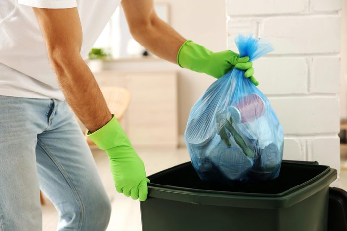 Man taking out trash and cleaning garbage can in bright neon green gloves