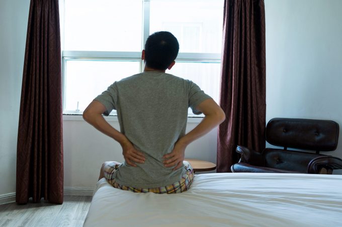 Man sitting on the edge of bed with backache