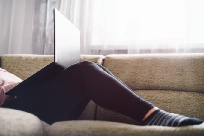Young Woman Using Laptop While Resting On Sofa At Home