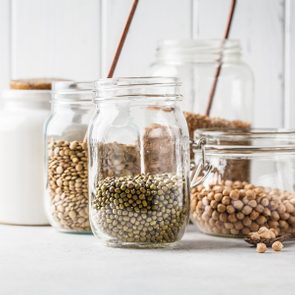 Various legumes: beans, chickpeas, buckwheat, lentils in glass jars on a white background. Healthy vegetarian food, vegetable protein, plant based diet concept.