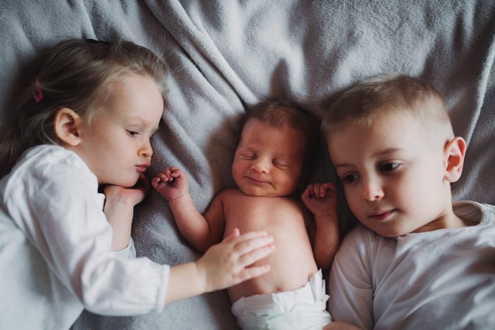 A view from directly above of two toddler children and a newborn baby brother or sister at home.