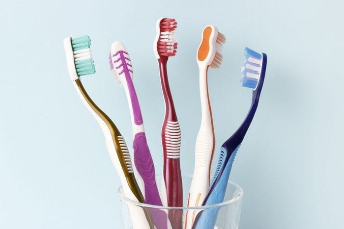 Multicolored toothbrushes in a glass cup front view, blue background