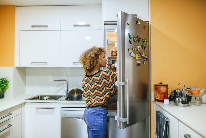 Young woman with curly hair opening the fridge in kitchen
