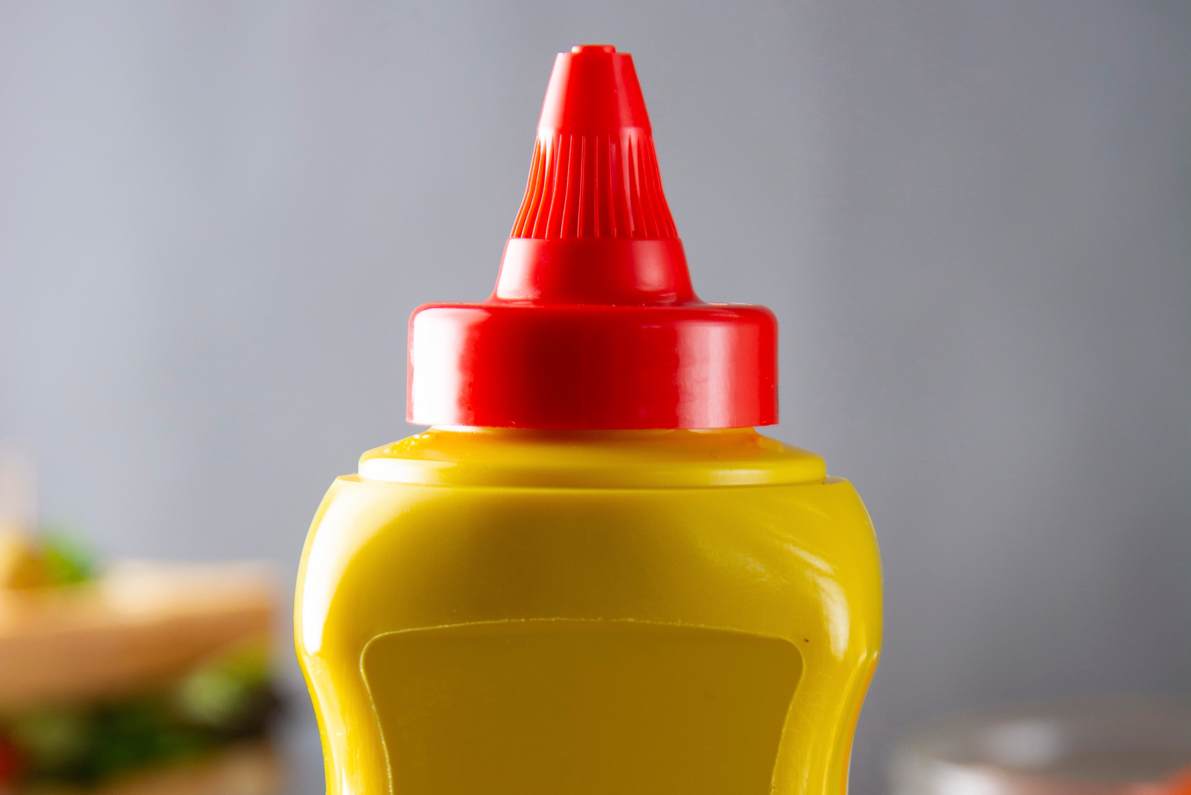Yellow mustard squeeze bottle container with no label. Breakfast sandwich on background. Food product.