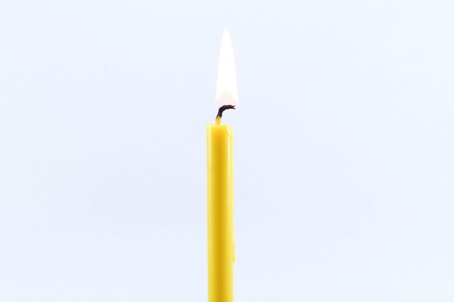 Close-Up Of Burning Candle Against White Background
