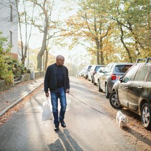 Full length of elderly man holding shopping bag walking with dog on road during autumn