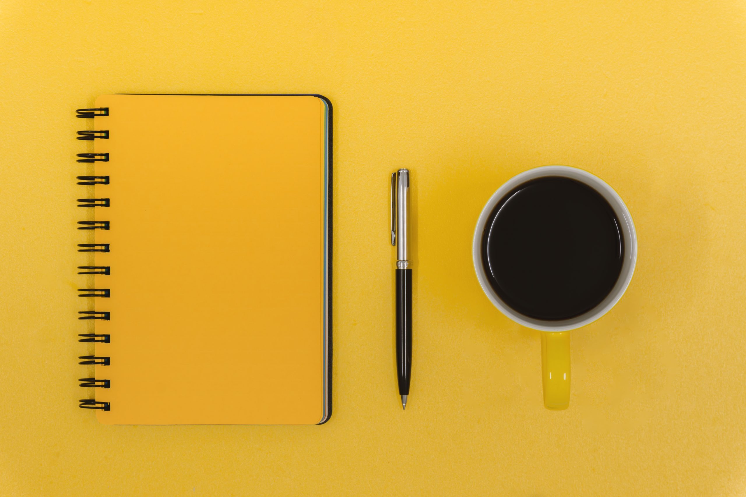 Notepad, Pen and Coffee Mug on Yellow Work Desk