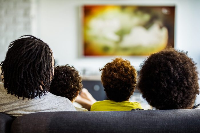 Back view of a family watching TV in the living room.