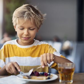Little boy eating breakfast crepes with fruits