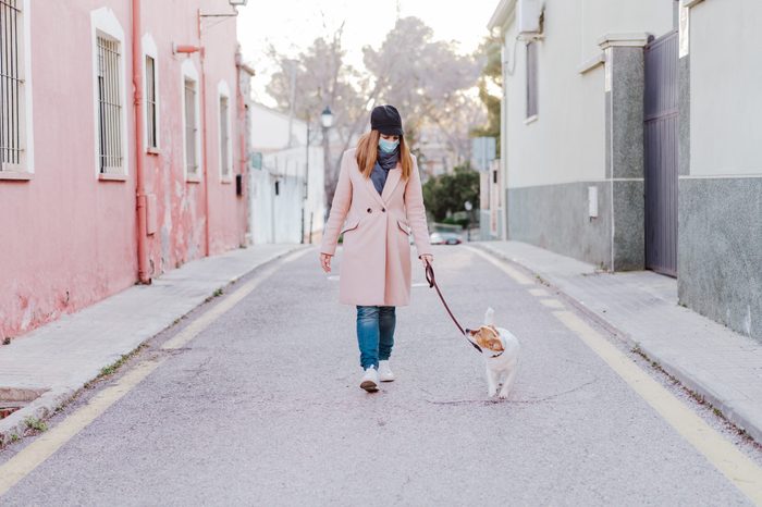 caucasian woman in the street wearing protective mask and walking with her dog. corona virus concept