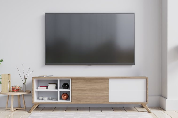 TV on the cabinet in modern living room with plant on white wall background.