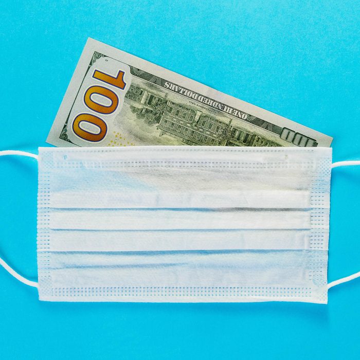 one hundred dollar bill under a surgical mask. blue background