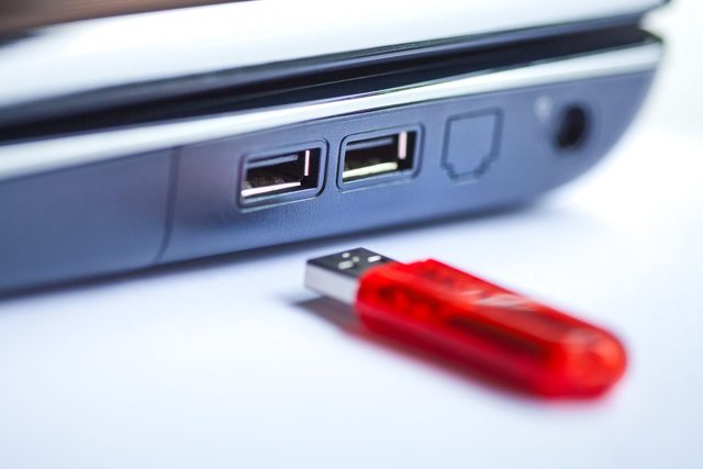 A red USB stick near a laptop, close up with narrow focus.