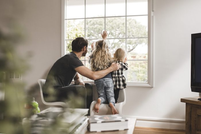 Father with daughters looking through window at home