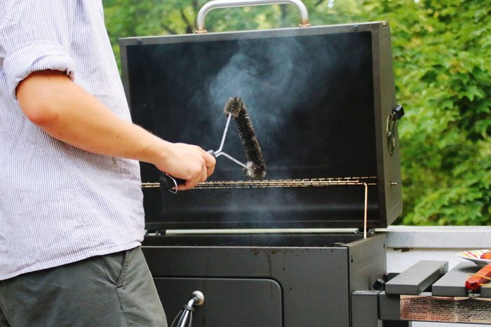 Midsection Of Man Cleaning Barbecue Grill With Wire Brush
