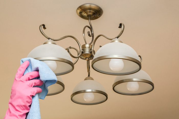 Hands with pink rubber gloves cleaning hanging light with blue rag