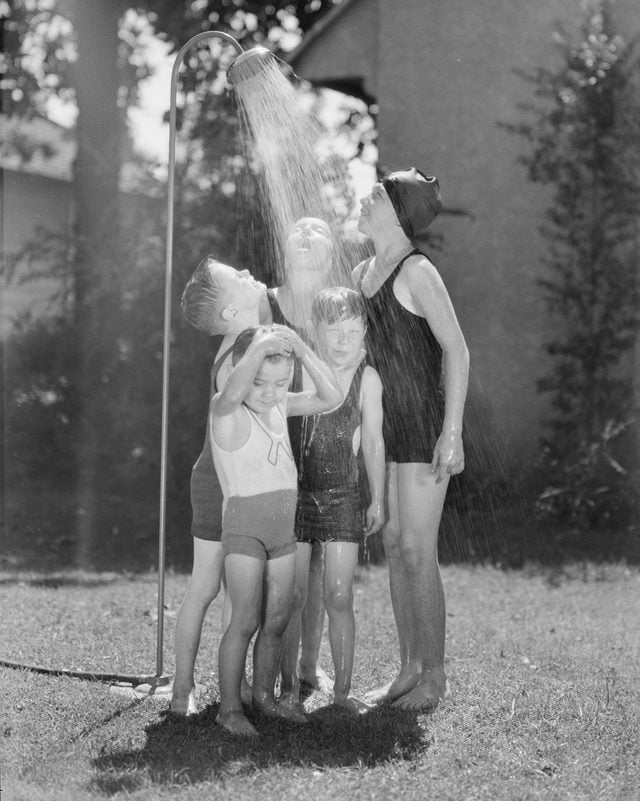 Children in bathing suits outside standing under a lawn shower, The May Company, Southern California, 1931.