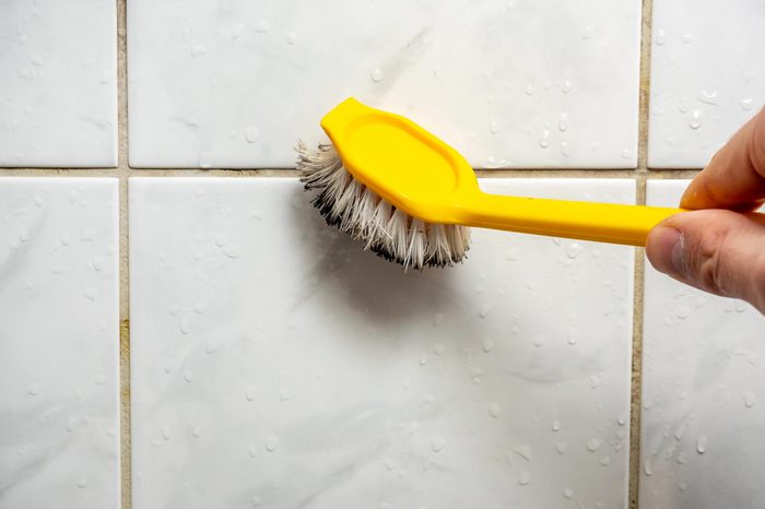 close up of a hand Cleaning dirty tile with a yellow brush