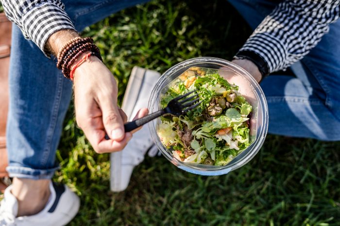 Man sitting on a meadow eating mixed salad, partial view