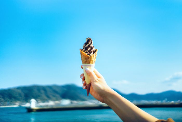 Cropped image of woman's hand holding ice-cream by the sea against clear blue sky