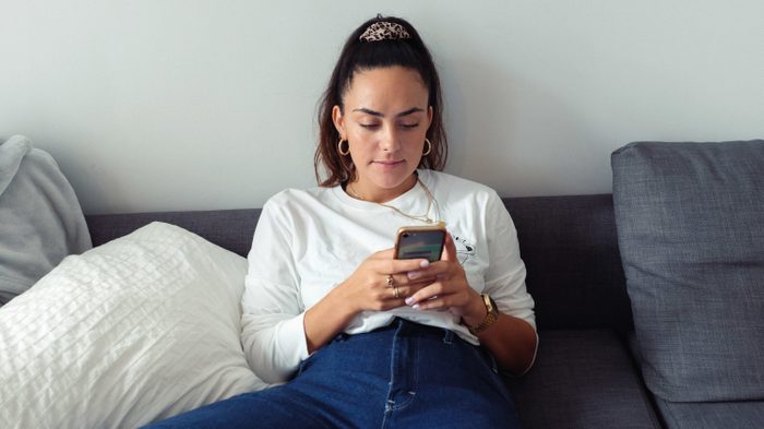 Young Woman Using Mobile Phone While Sitting On Sofa At Home