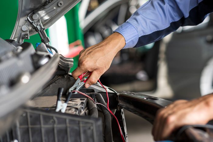 Professional car mechanic using jumper cables to start a car battery.
