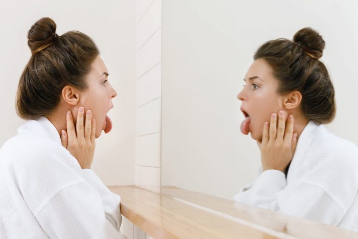 Woman looking on her tongue in the mirror