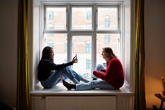 Young female roommates using smart phones at apartment window