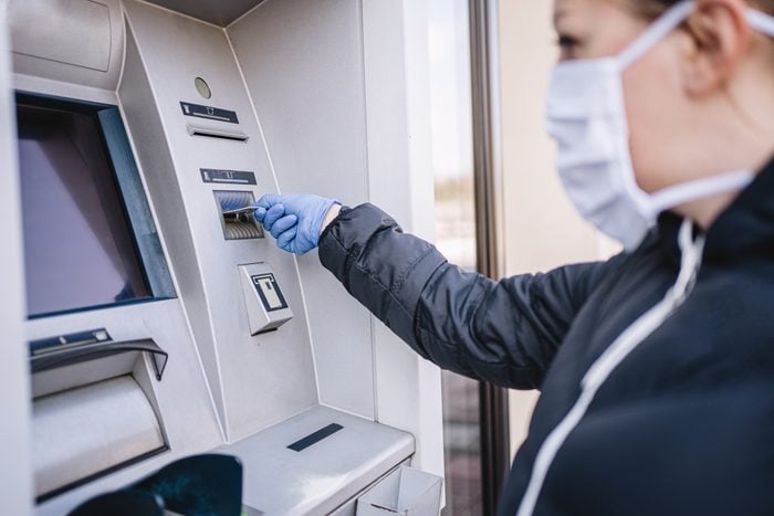 Woman with gloves and a face mask on a bank ATM using a credit card during a coronavirus pandemic
