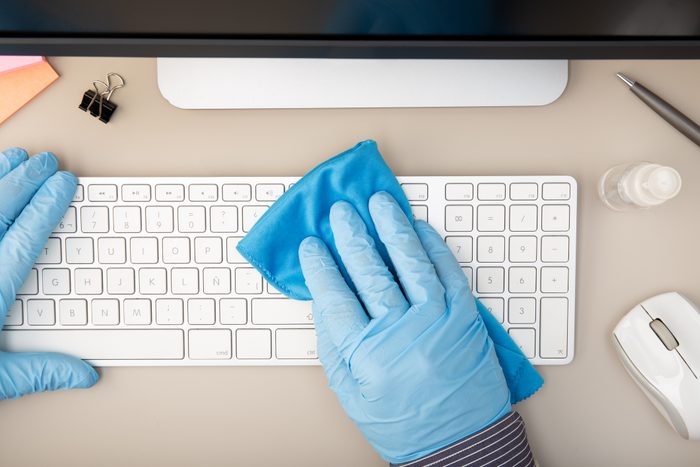 Cropped Hands Wearing Gloves Cleaning Keyboard On Desk