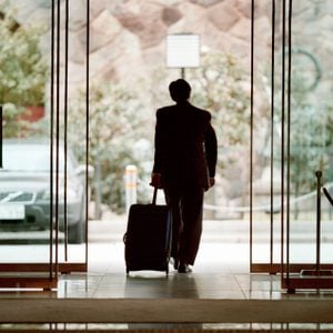 Businessman leaving lobby with luggage, rear view