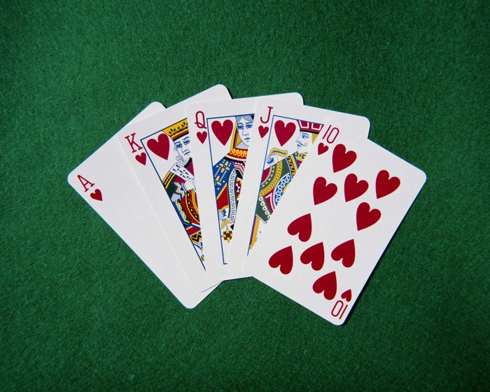 Royal flush hand of cards, hearts suit, on playing baize, close-up