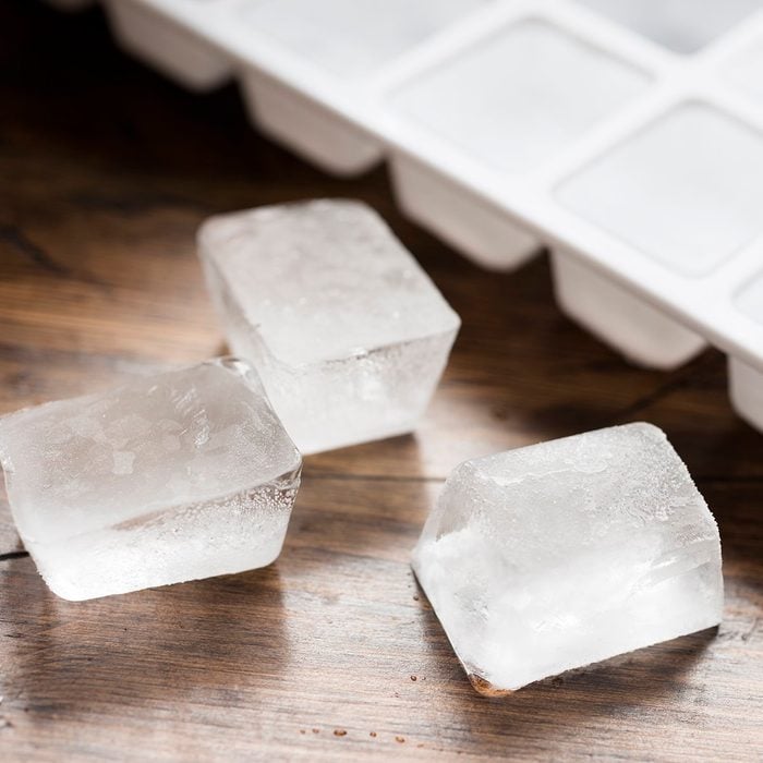 Ice cube tray filled with ice cubes and three lose ice cubes against dark wood.