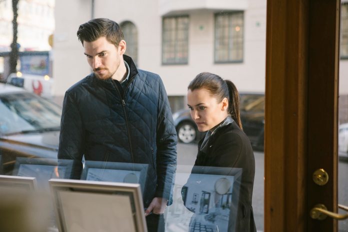Young couple looking at picture frames on display seen from office window