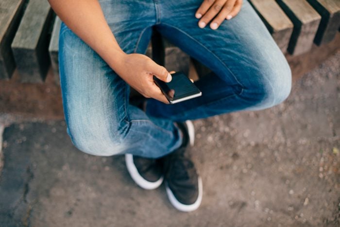 Low section of young man using smart phone while sitting on bench in city