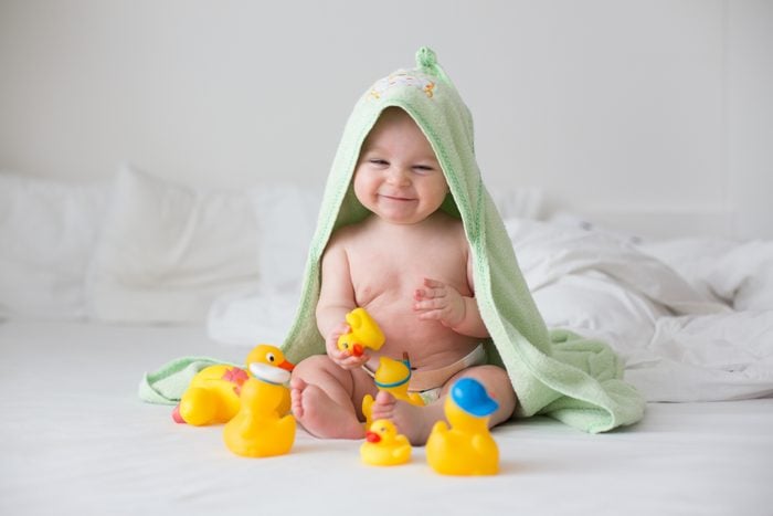 Cute little baby toddler boy, playing with rubber ducks after bath in bed
