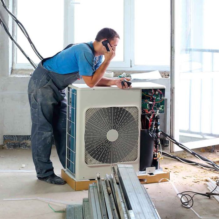 A worker sets air conditioner in apartment and talking on the phone